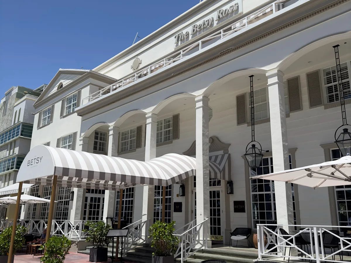 The image presents a white building with striped awnings and outdoor seating under a clear blue sky, suggesting a leisure or hospitality establishment.