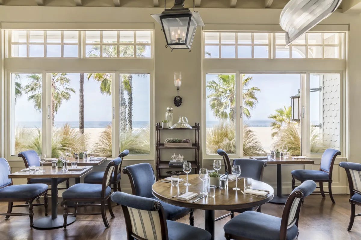 elegant restaurant dining room with round tables and blue chairs overlooking the beach