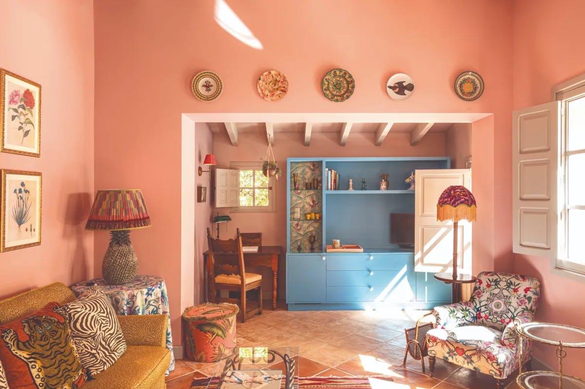 a charming, sunny living room with pink walls and brightly patterned furniture and pillows