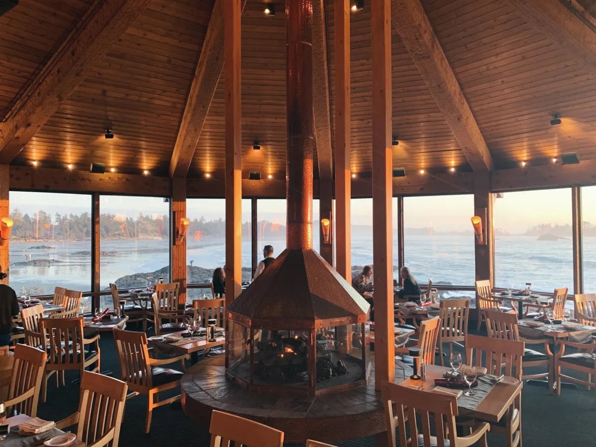 Restaurant with wooden beams and pillars and floor-to-ceiling windows looking out to the ocean