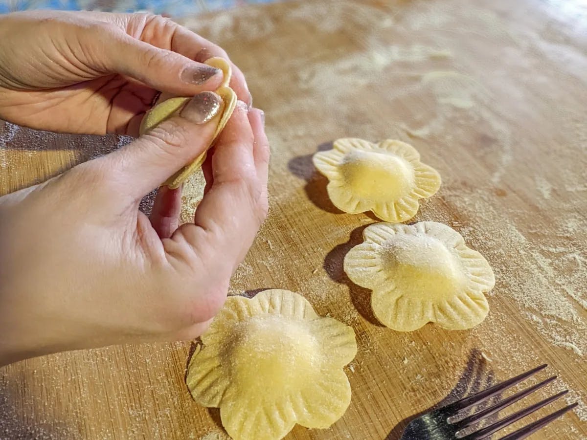 Hands preparing flower-shaped pasta on a floured surface.