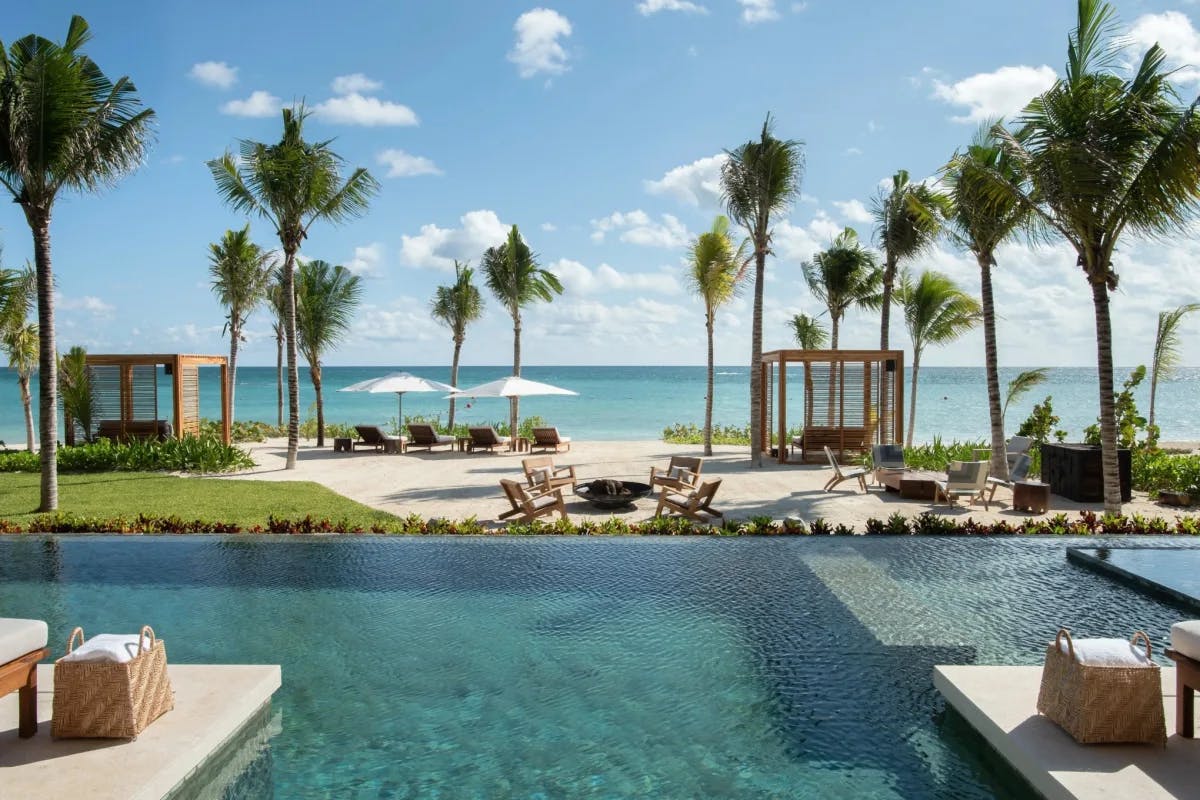 infinity pool looking at beach and sea beyond with cabanas and tall palm trees