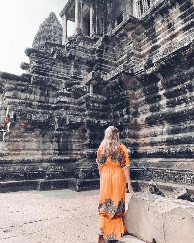 Advisor posing for an image in front of ancient ruins in an orange dress during the day time. 