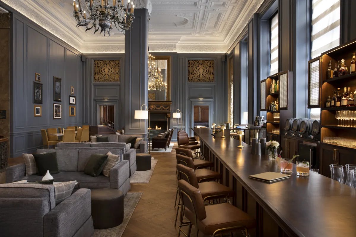 A hotel lounge and bar with chandeliers and blue paneled walls and pillars.