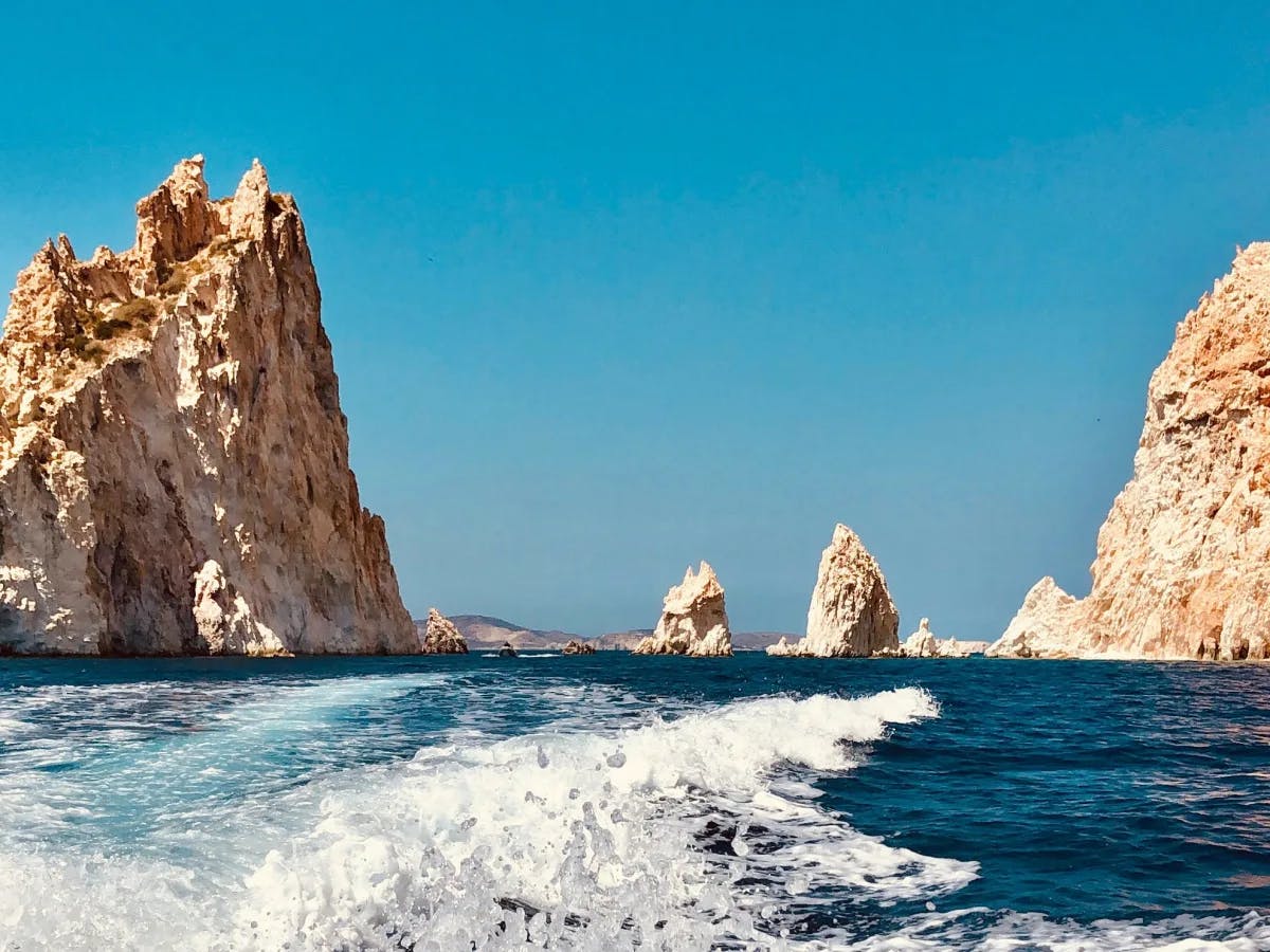 White craggy mountain outcroppings on either side of a boat's wake on the blue sea.