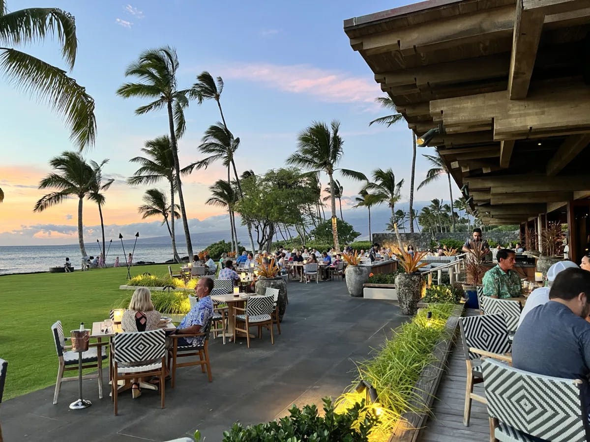 An outside eating area of a restaurant with lots of palm trees under a sunset sky