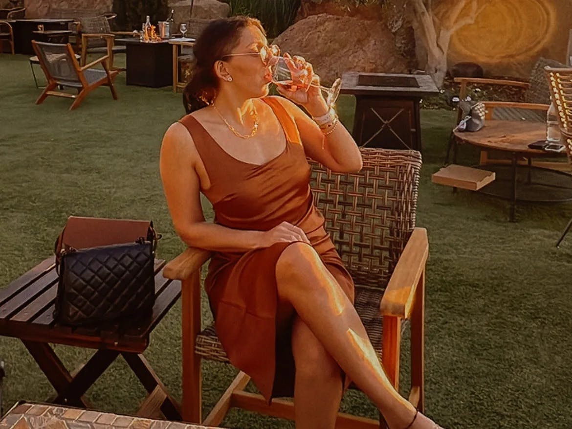 A woman sitting outdoor drinking wine. 