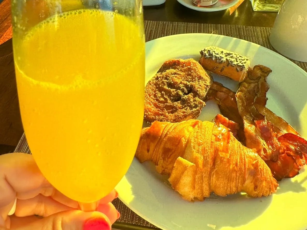 A glass of orange juice and a croissant, bacon and other breakfast foods on plate.