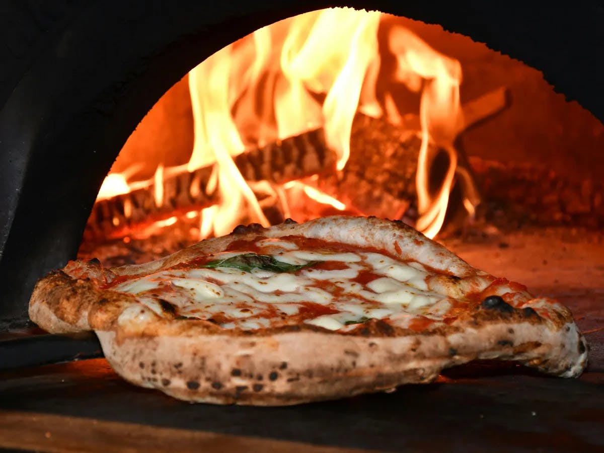 A delicious pizza with a golden crust and fresh basil, straight out of a flaming wood-fired oven. 