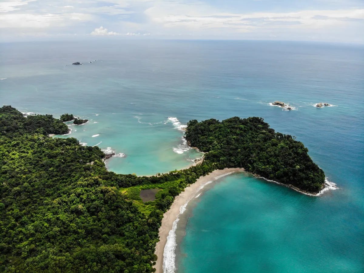 An aerial view of a narrow strip of land surrounded by beach and ocean on both sides with lush forest all around