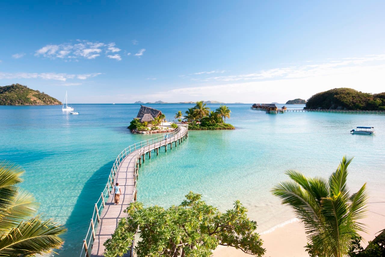 A bridge over bright blue water leading to an island resort 