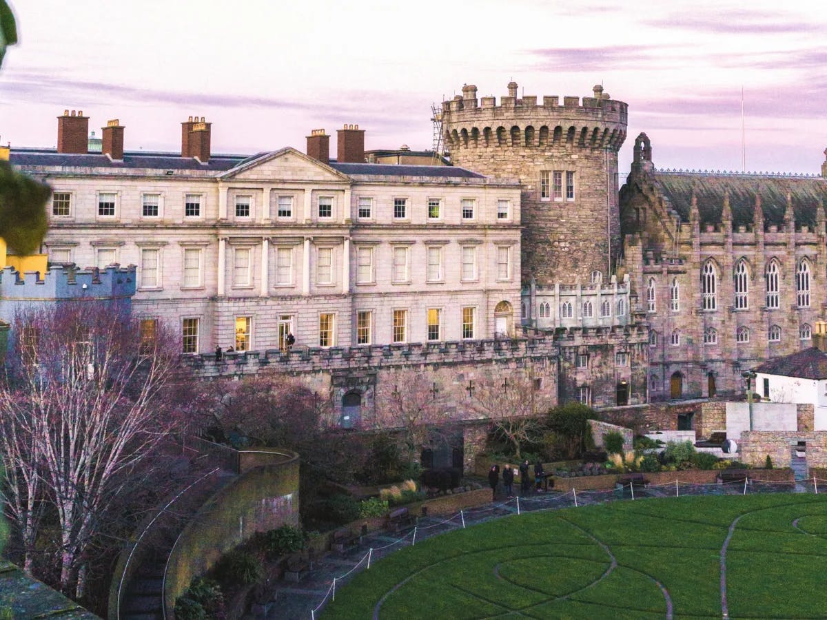 Dublin Castle, a historic stone building with battlements, next to a manicured garden during twilight.