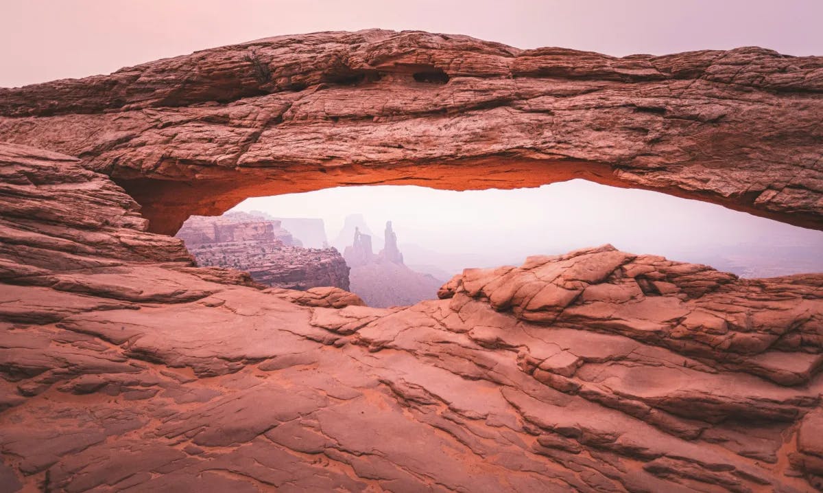 Looking through a brownish/red rock arch at other rock formations in the distance.