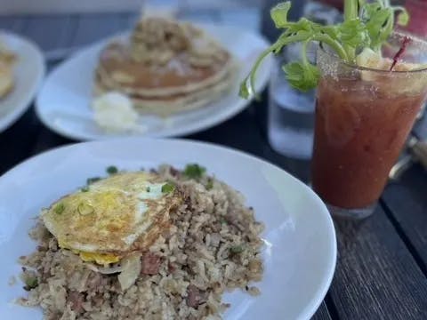 A picture of fried rice with an egg on top and a bloody mary on a table.