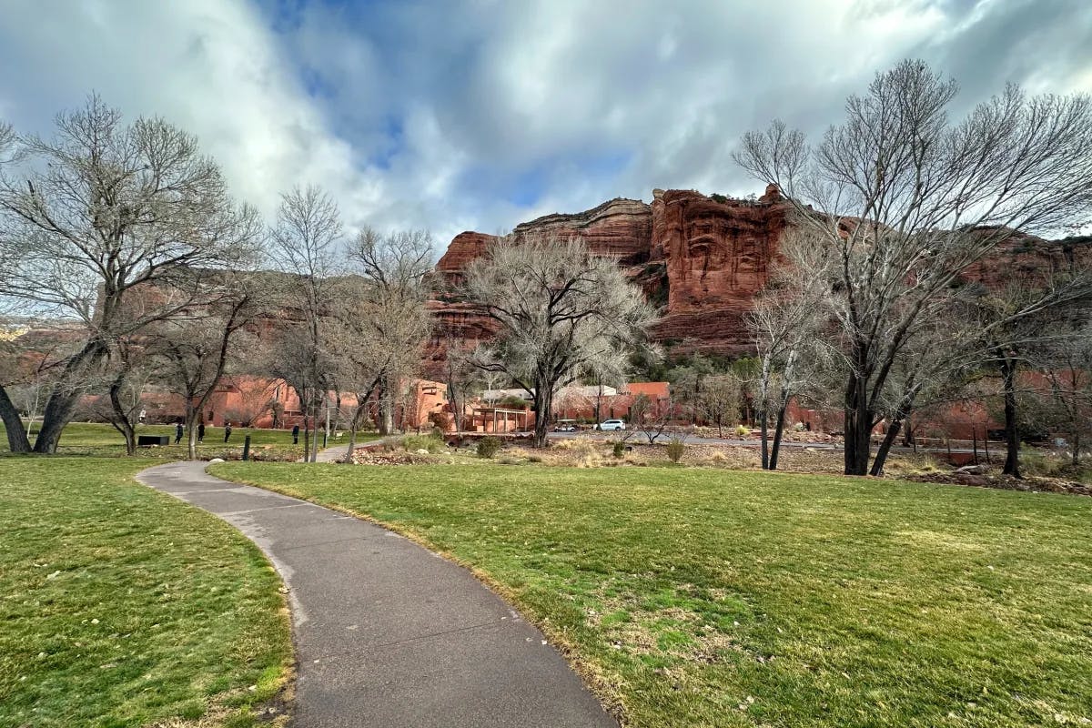 A path through a lawn in front of tall mountains and trees