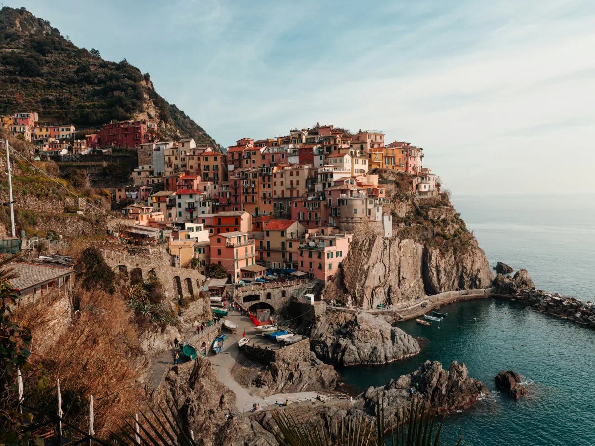 This captivating image showcases a colorful coastal village perched on rugged cliffs, overlooking a tranquil sea. The multi-hued buildings cling to the steep terrain, creating a picturesque scene.