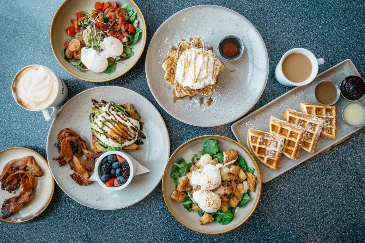 A spread of brunch items plated beautifully with two coffee beverages.