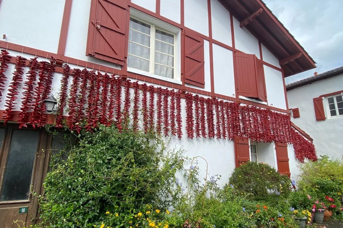 A traditional white house with red shutters and trim, with green hedges out front.