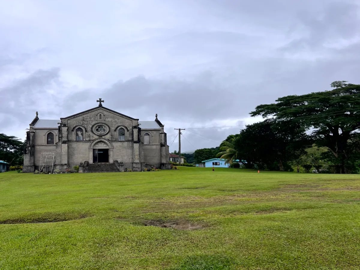 An old stone church set amidst a green landscape under a cloudy sky.