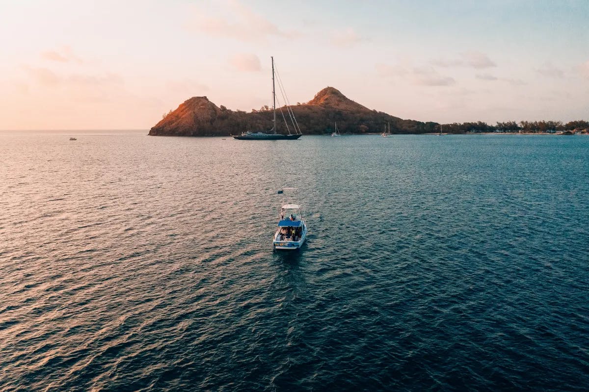 A boat sailing in a sea with pointed small hills at the back. 