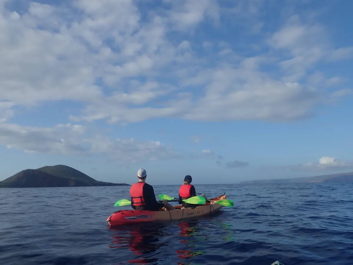 Two people sitting in a tandem kayak on the ocean, facing away from the camera.