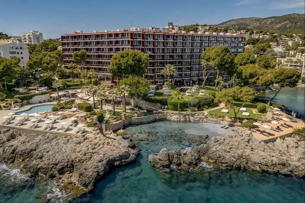 pink hotel on a seaside ledge with a pool and lawn area on rocks leading to the sea