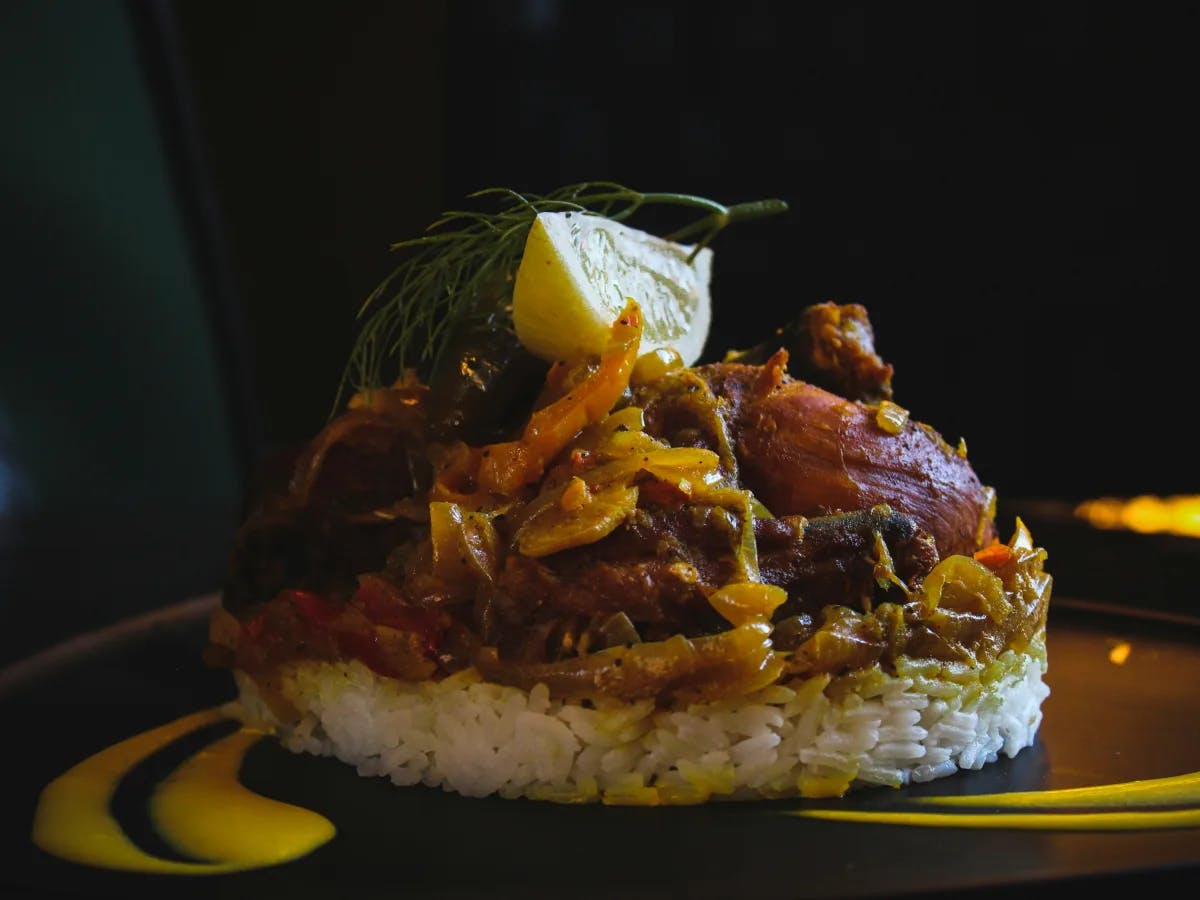 The image depicts a savory dish of rice with meat, garnished with lime and herbs, served on a dark backdrop.