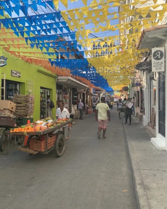 A street with colorful flags up and a fruit vendor. 