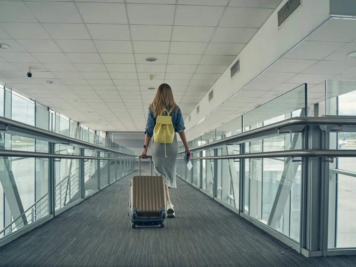 A person walks through an airport corridor, pulling a suitcase and carrying a backpack, suggesting travel or transit.