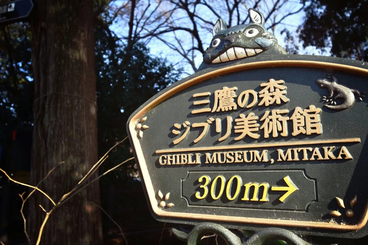 A picture of a directional sign for the Ghibli Museum in a park.