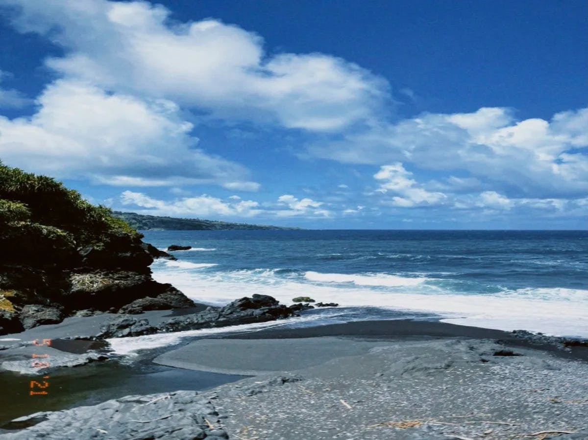 A serene coastal landscape with a blue sky, fluffy clouds, and a rocky shoreline leads to a calm sea.