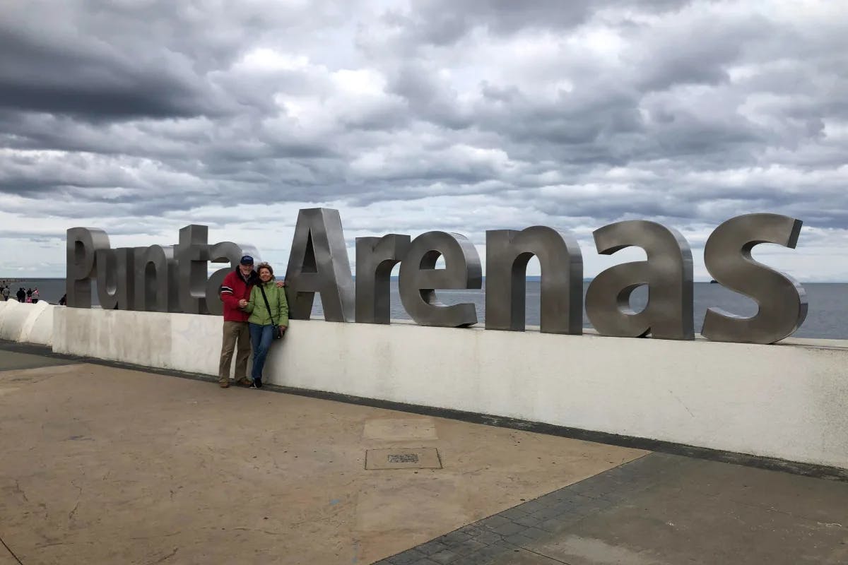 A couple standing in front of a large sculpture reading "Punta Arenas" outside on a cloudy day