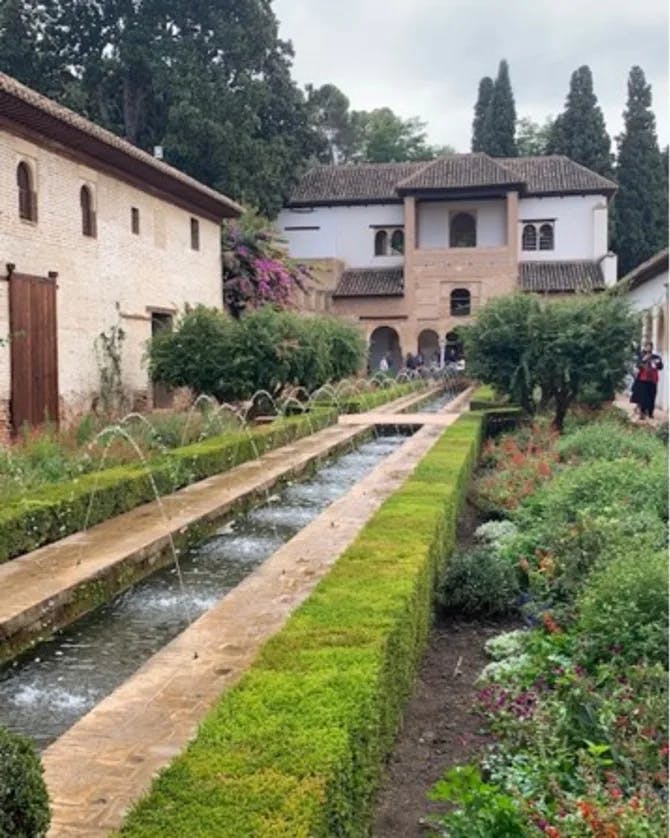 A garden with a large water feature outside of a chateau-style house.