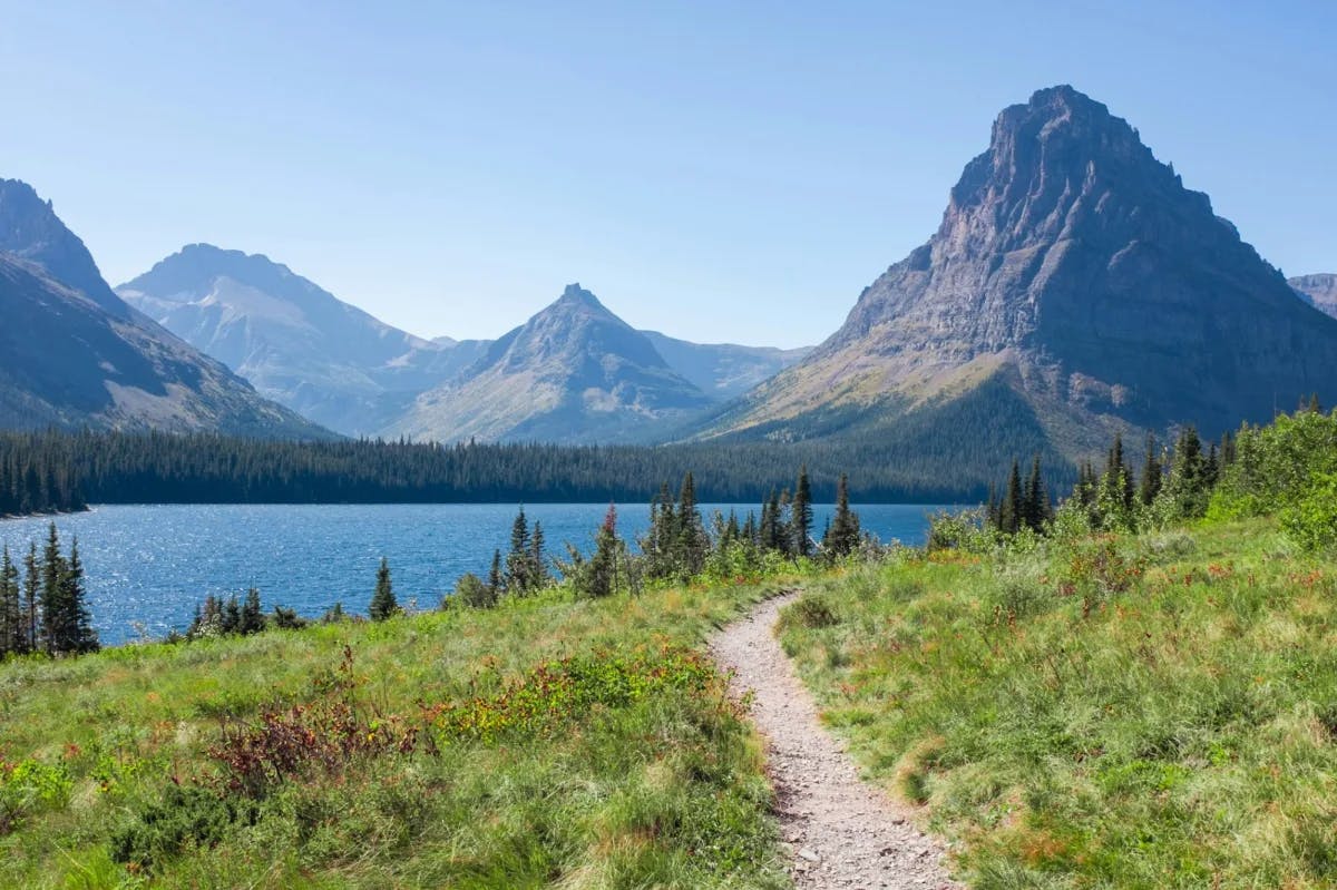 hiking trail leading to a mountain lake with towering mountains in the background