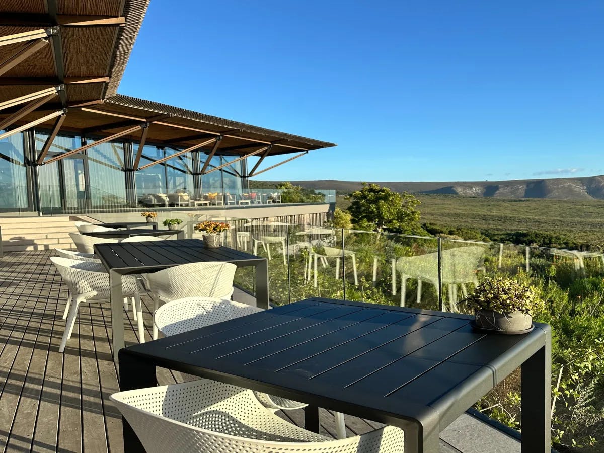 An outdoor patio with black tables and a wood roof overlooking a field.