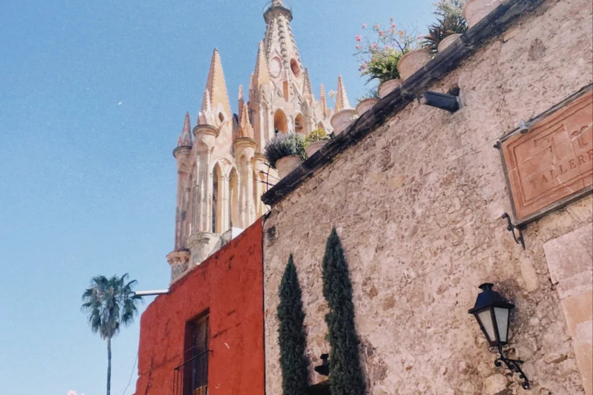 A street view of a red brick building next to a magnificent building with ornate carvings and towers known as the  Parroquia de San Miguel Arcángel. 