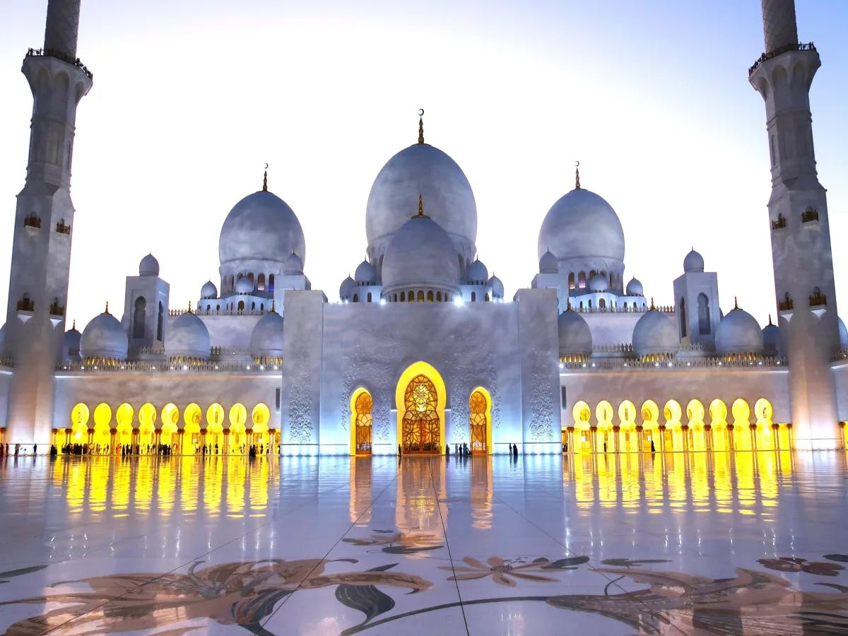 A picture of a white-colored mosque with yellow lights.