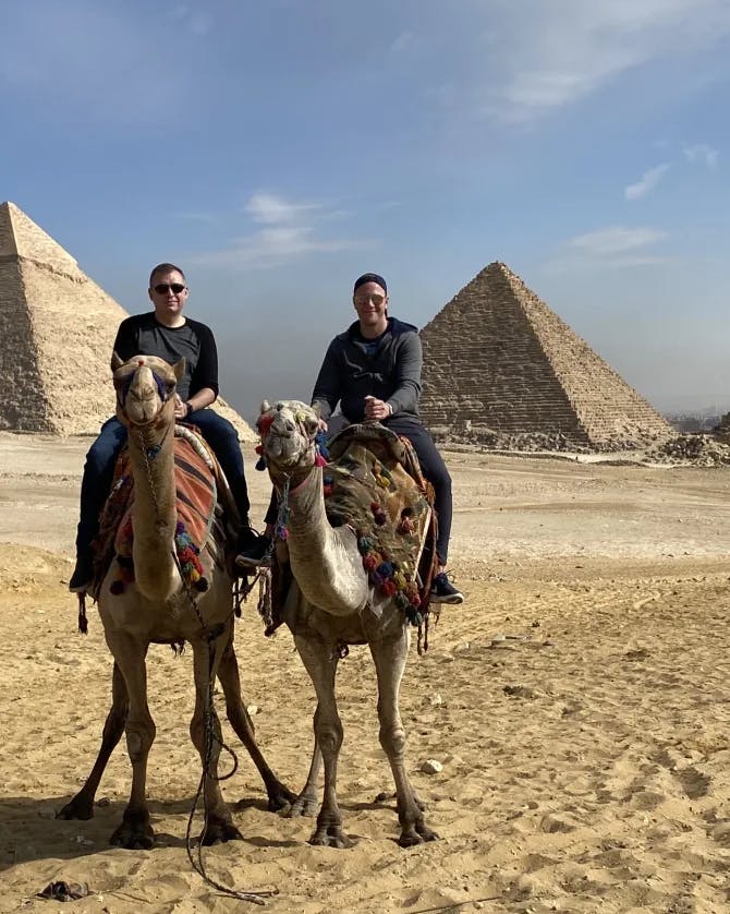 Anthony and a friend riding a camel in front of the Pyramids of Giza.