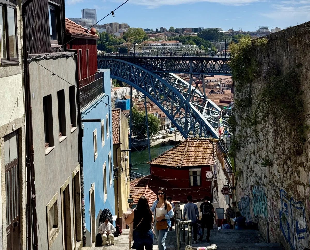 A stone alleyway on a hill leading down towards water with a blue bridge over it