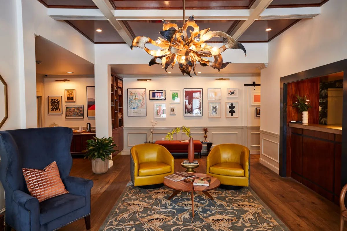 a stylish hotel lobby with a funky gold chandelier, two yellow chairs, and an upholstered blue armchair