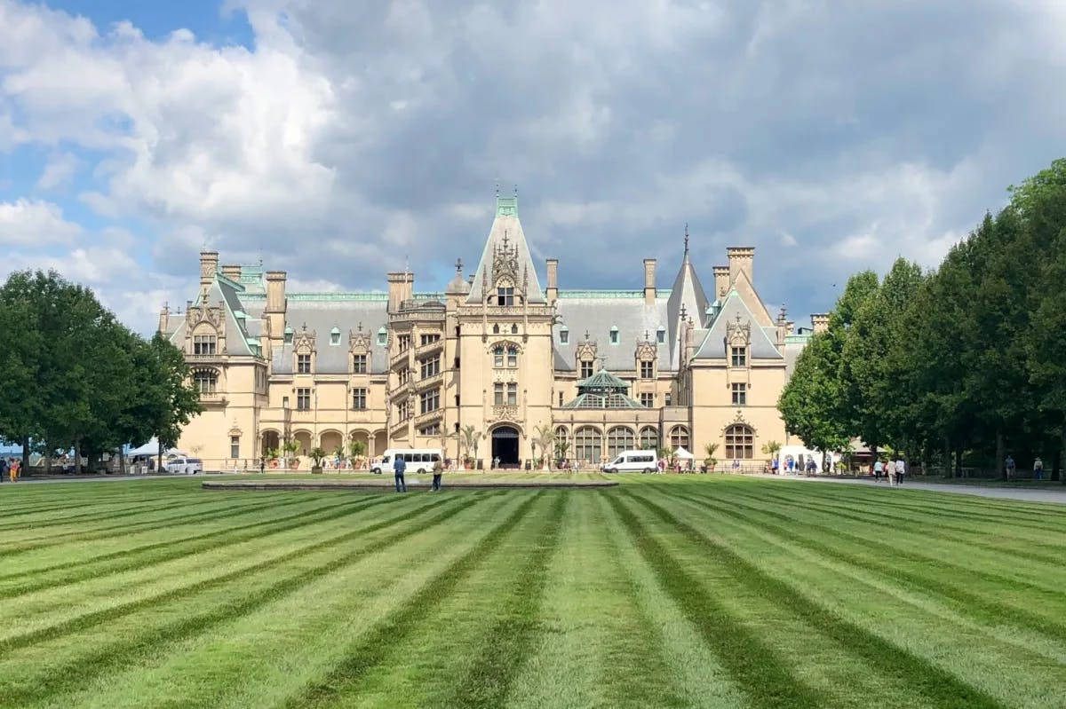 manicured lawn leading up to a grand mansion with pointed towers and turrets with a blue sky