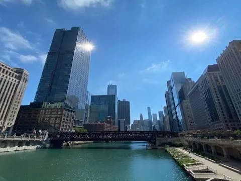 The image captures a cityscape with skyscrapers by the river, bathed in sunlight under a clear blue sky.