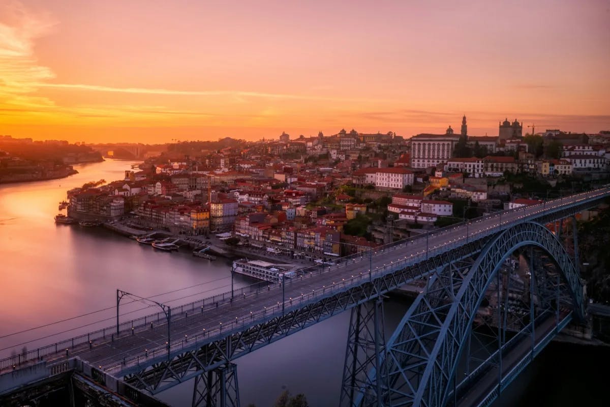 A view of the Dom Luís I Bridge over the Duoro River, with a view of Porto underneath a golden sunset.