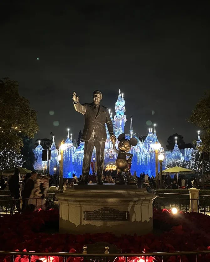 Picture of the Walt Disney statue at night in front of the lit up castle