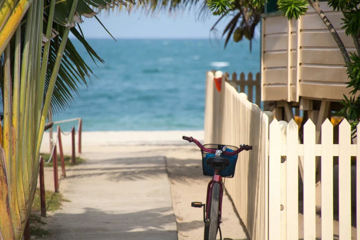 A view of a path leading out to a beach with a white picket fence and bike leaning against the fence