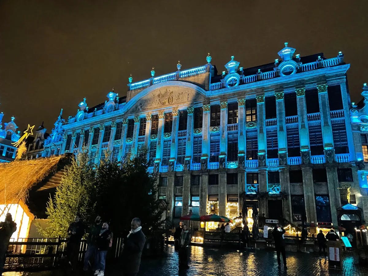 A historic building in Brussels’ Grand Place bathed in vibrant blue light at night, accompanied by a lively night market