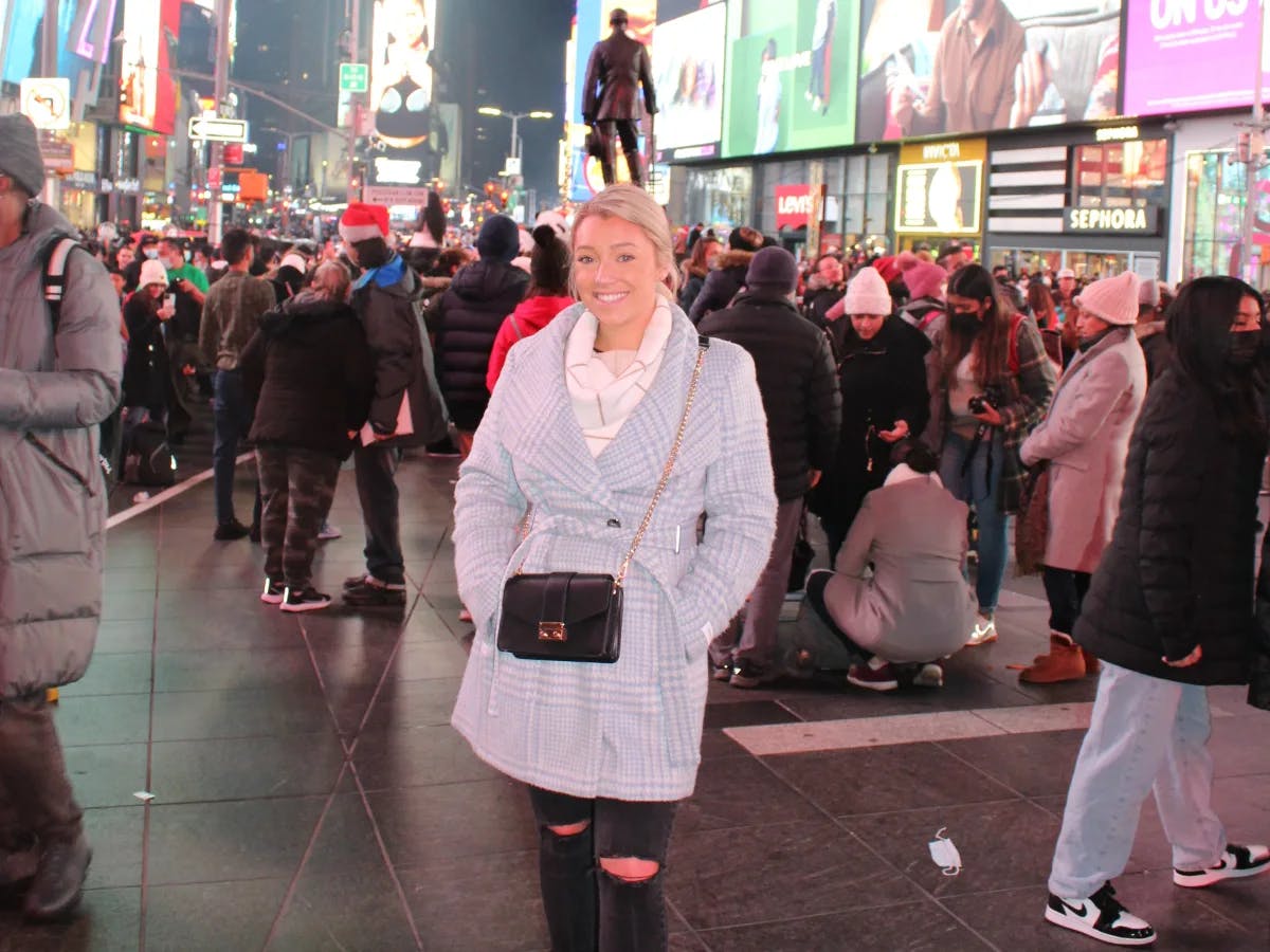 A woman posing in a light blue jacket in the middle of Times Square with hundreds of tourists in the surrounding areas. 