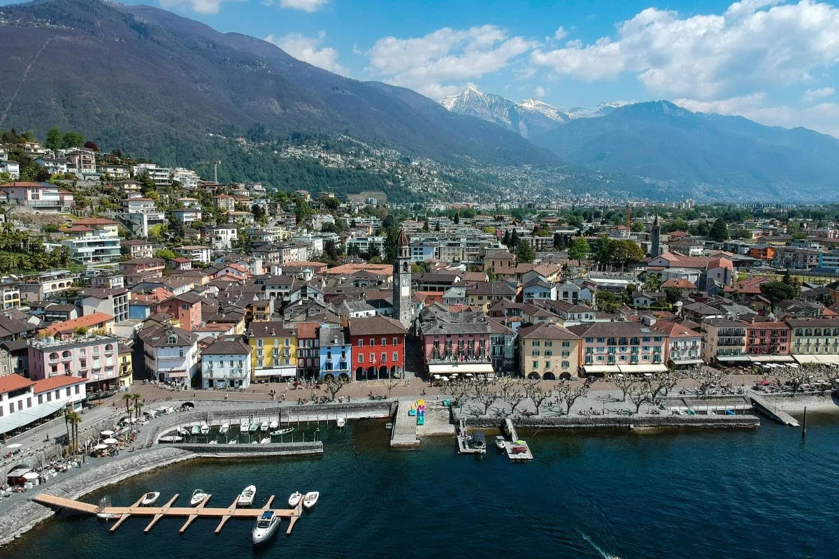 An aerial view of the lake, village, mountains, and sky in Ascona during the daytime.