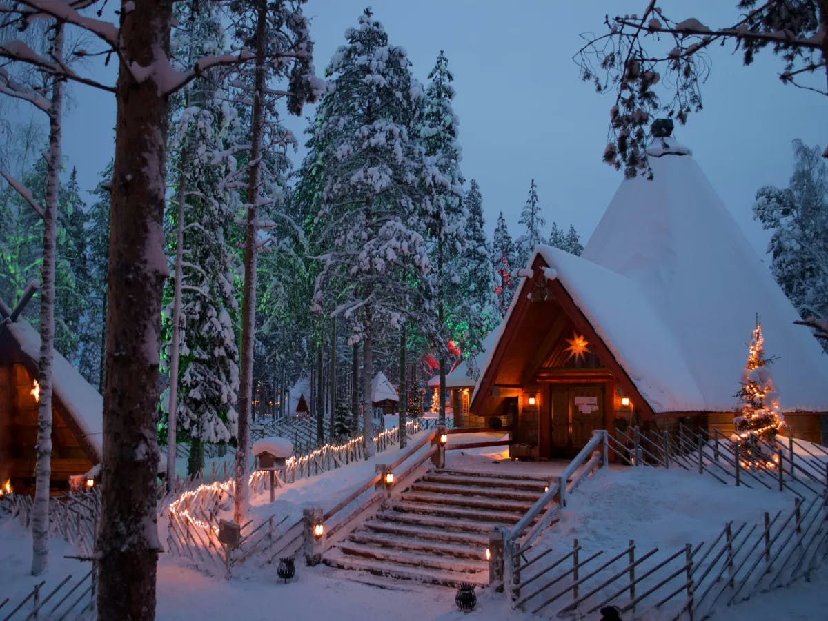 A cozy winter scene with a warmly lit cabin, a Christmas tree and a teepee amidst a snowy forest.