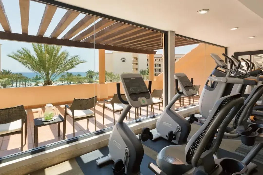 Fitness equipment fills a room with floor-to-ceiling windows looking out over San Jose del Cabo's beach